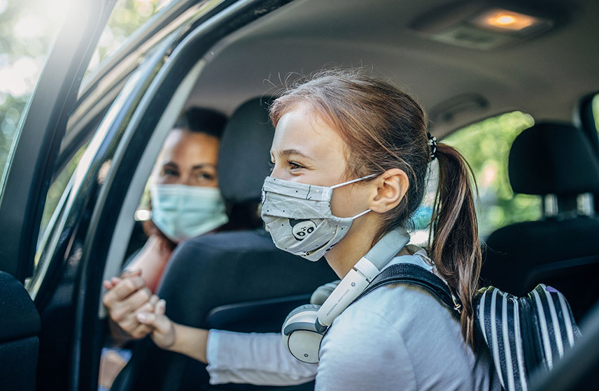 Mom and daughter in masks holding hands before daughter gets out of car.